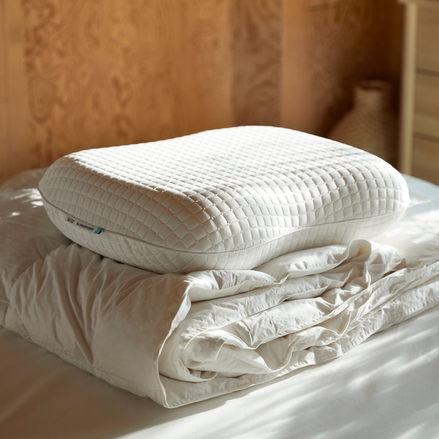 Ergonominen KLUBBSPORRE-tyyny ja lämmin FJÄLLARNIKA-untuvapeitto sängyn päällä.