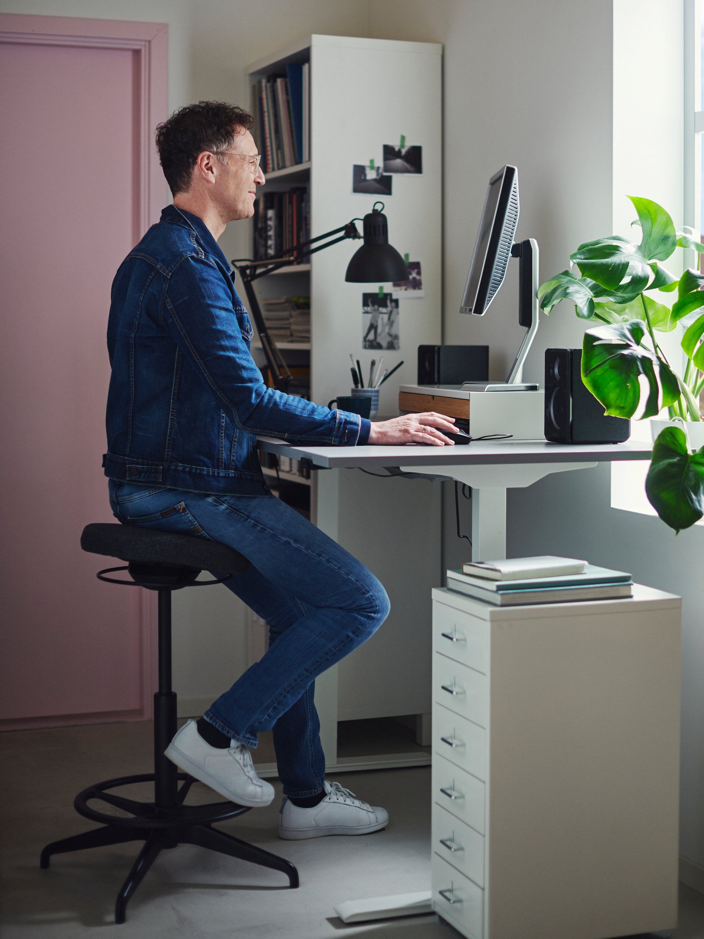 Someone is sitting on a black stool at a standing desk.