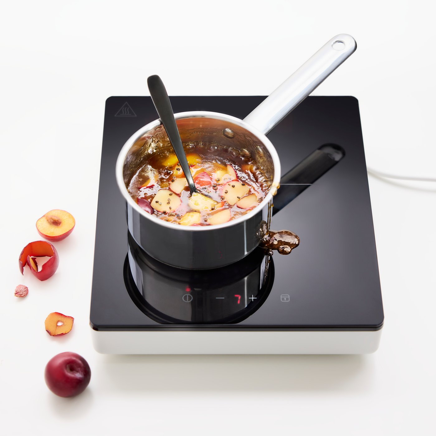 A portable TILLREDA induction hob with a pot of apple chutney, seen from above. Next to the hob, some apples.
