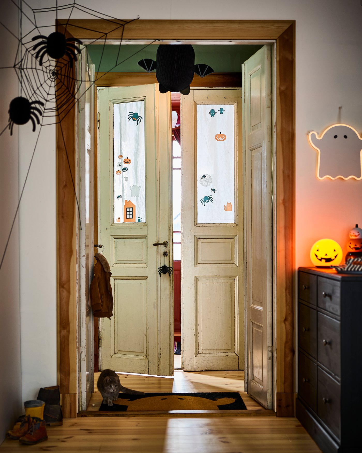 En inbjudande hall dekorerad för Halloween med spindelnät, en hängande fladdermus, ett neonskylt-spöke och en lysande pumpalykta som skapar en spöklik men rolig stämning.