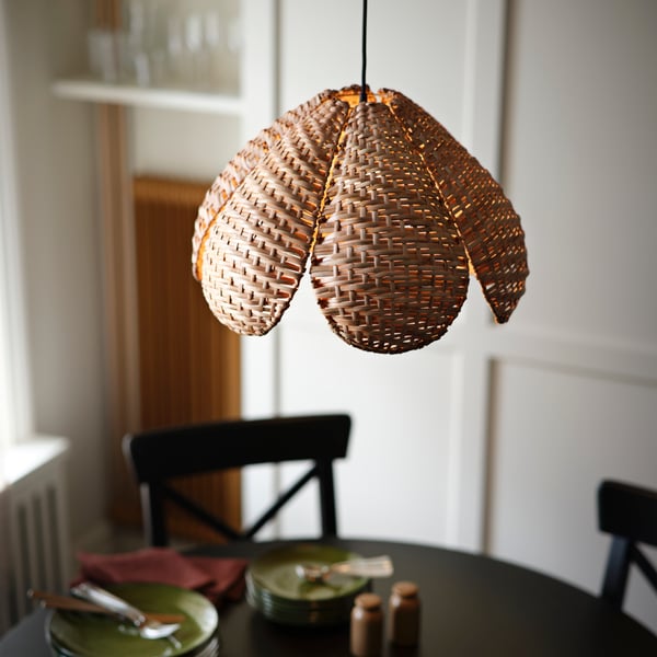 A warm-toned SANDKORN pendant lampshade featuring a woven design, hanging above a dining table with green plates.