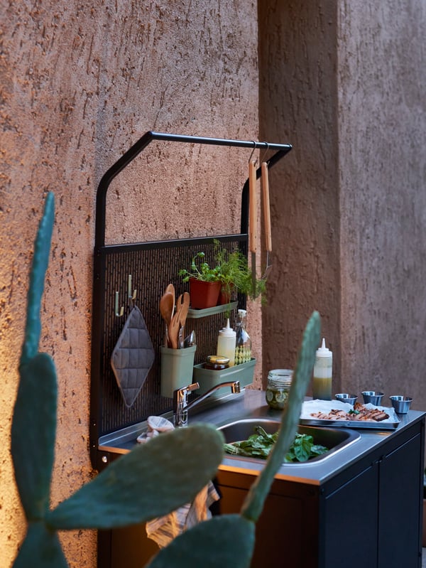 Un mueble para lavapatos de exterior GRILLSKÄR montado en una pared con un espacio para volgar y almacenar artículos de asado.