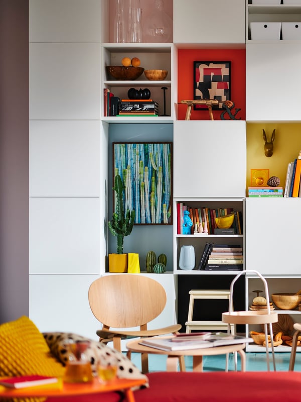 A living room where a wall-covering BESTÅ unit creates a checked pattern of white fronts and colourful display storage.