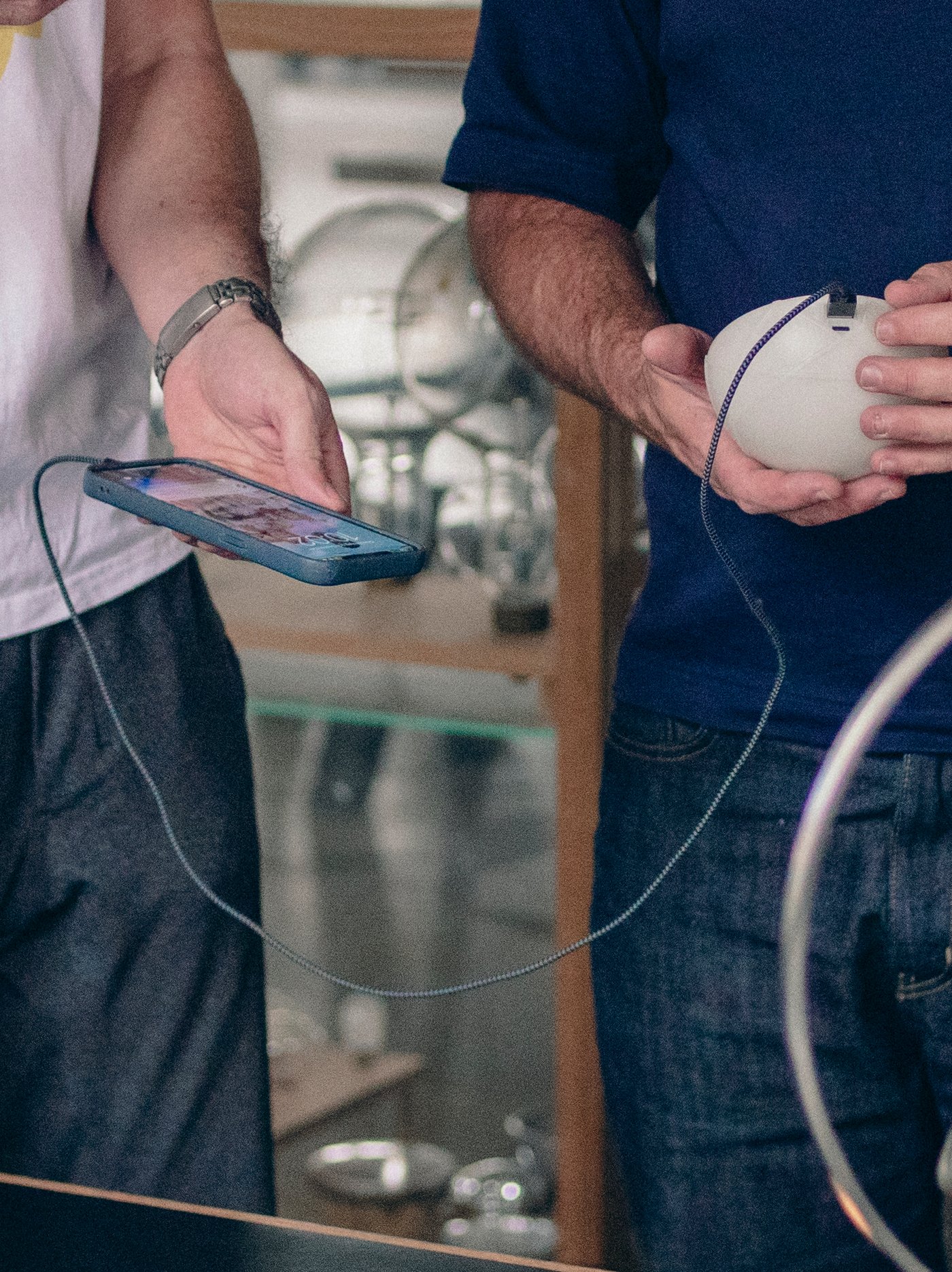 Dua orang berdiri di belakang meja sedang mengecas telefon dengan bantuan lampu meja berkuasa solar LED SAMMANLÄNKAD.