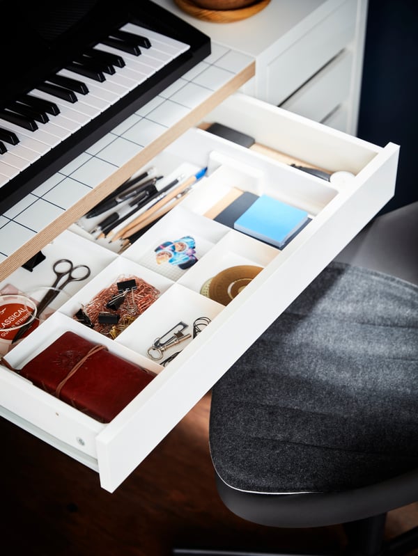 A KUGGIS eight-compartment insert filled with desk accessories in the open drawer of a white-and-anthracite MICKE desk.