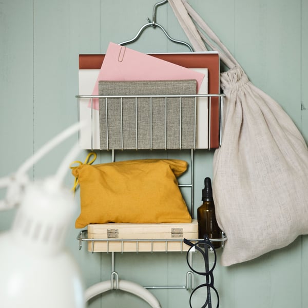 A zinc-plated KROKFJORDEN shower hanger on a green wood panelled wall holding books, spectacles and various other items.