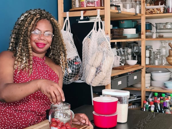 Nureen poserer med et glas med tomater og net fyldt med frisk frugt og grønt.