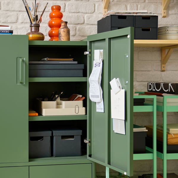 An IDÅSEN cabinet with one door open, showing anthracite paper boxes and a grey-beige KUGGIS desk organiser set.