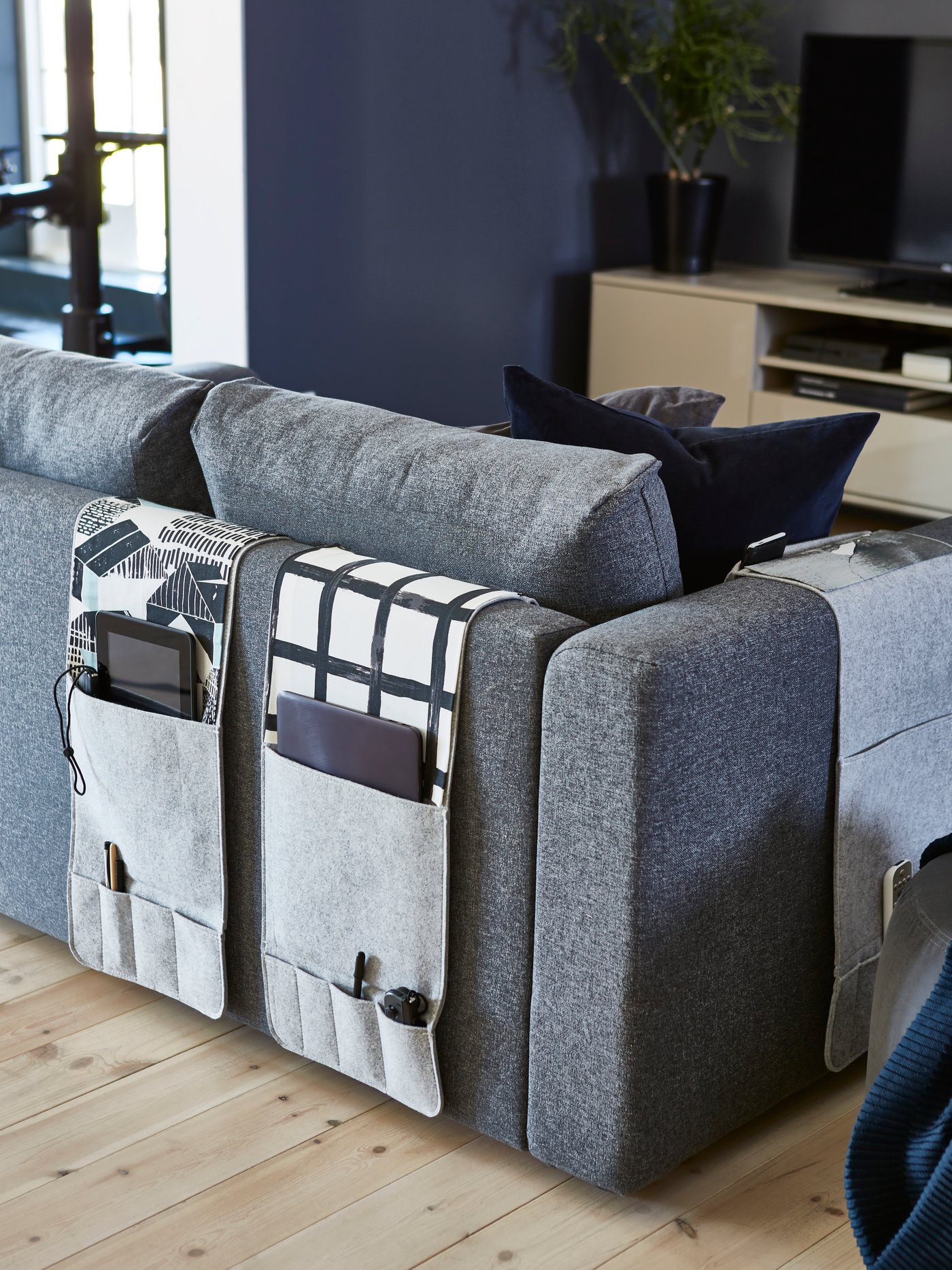 An IKEA KNALLBÅGE grey felt sofa organisers hang on the back of a grey sofa in this living room.