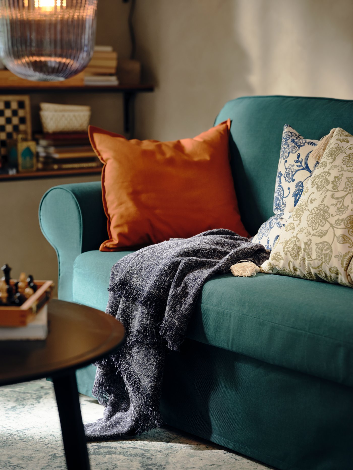 Cojines y una cobija descansan sobre un sofá cama VRETSTORP de color turquesa oscuro. Una mesa de centro negra KRAGSTA se encuentra al lado.