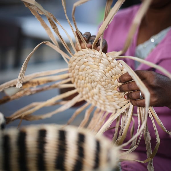 A person is handweaving the lid of a MÄVINN box with lid. The banana fibres sticking out makes it resemble the sun.