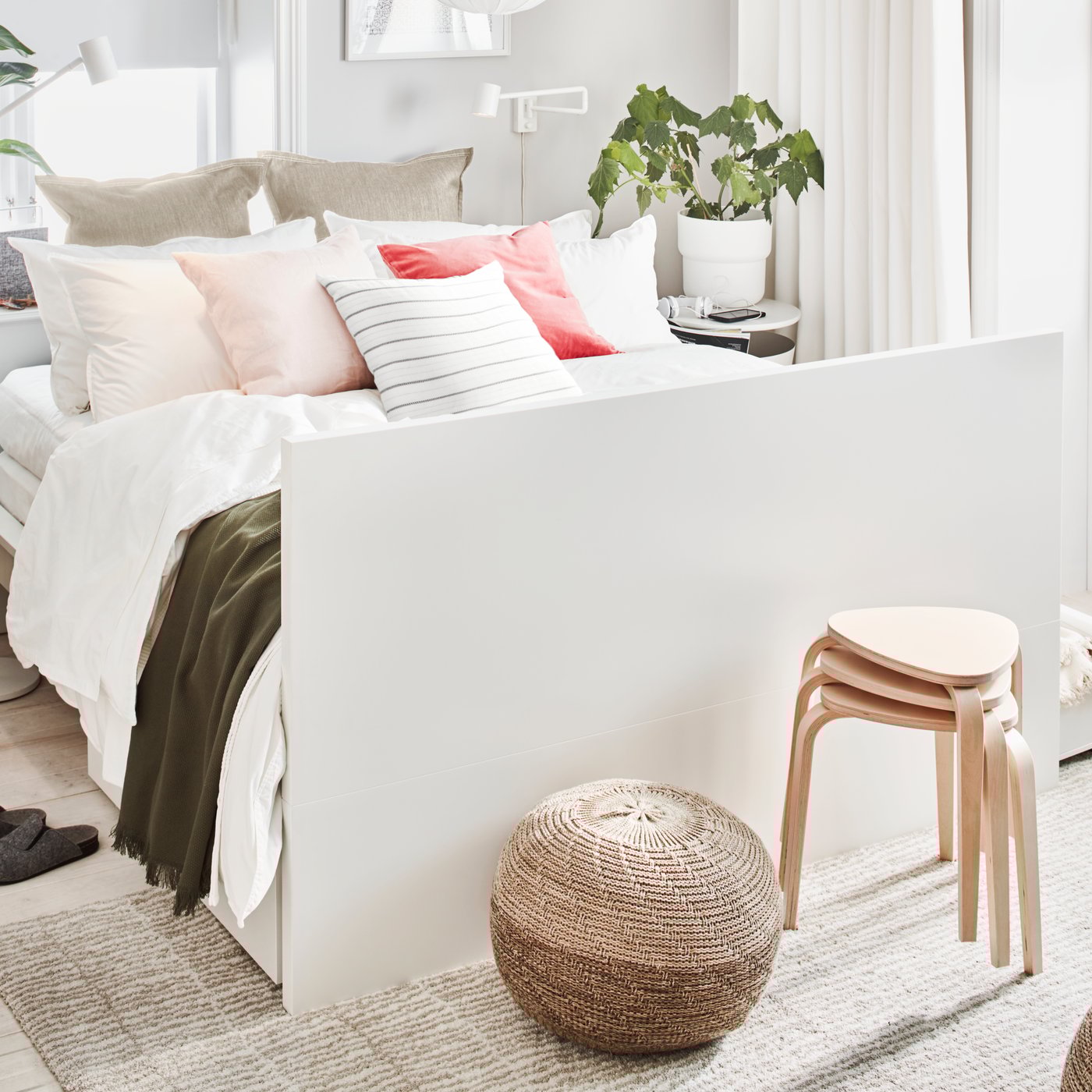 Ein MALM Bettgestell in Weiß mit zwei Schubkästen ist dekoriert mit mehreren Kissen. Das Kopfteil des Gestells dient hier als Fußende. Alles ist in luftig-leichtem Weiß gehalten.