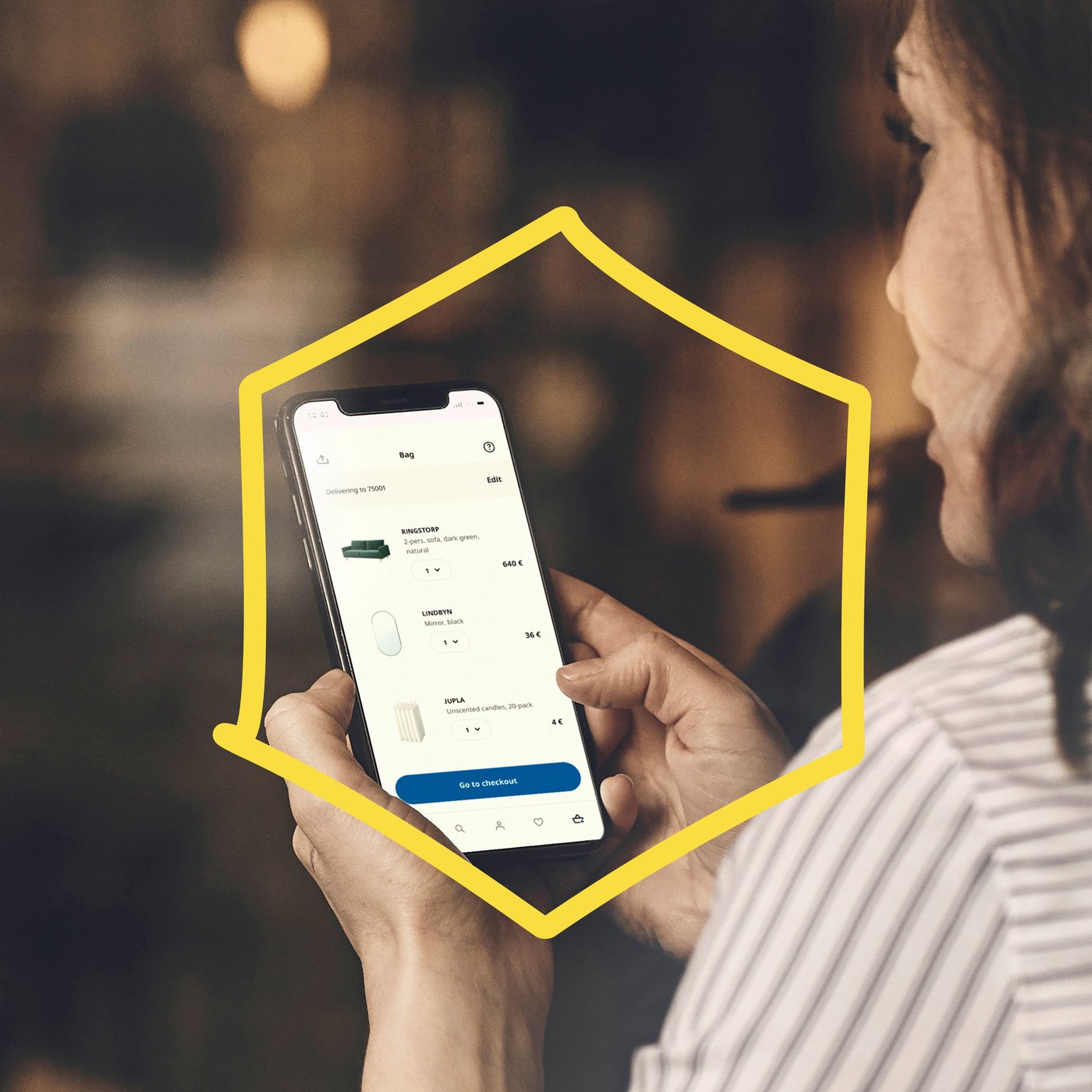 Osoba trzyma telefon z aplikacją zakupową IKEA, otoczoną żółtym konturem domu.