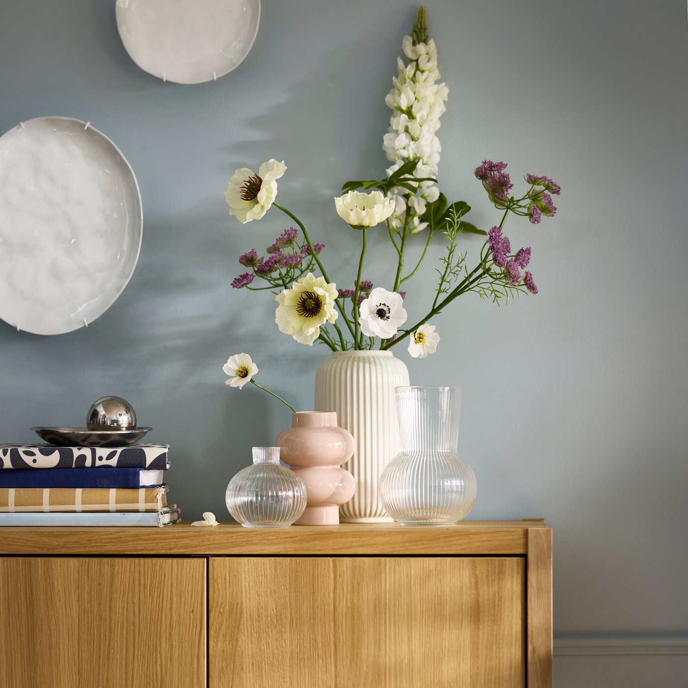Neatly arranged artificial flowers in a STILREN vase flanked by other decoration on top of a STOCKHOLM wooden cabinet.