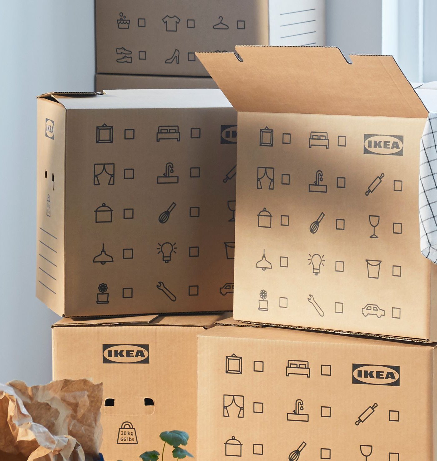 Stack of DUNDERGUBBE moving boxes in corner of a room with window plus SOCKERBIT storage boxes, FRAKTA bag and plants.