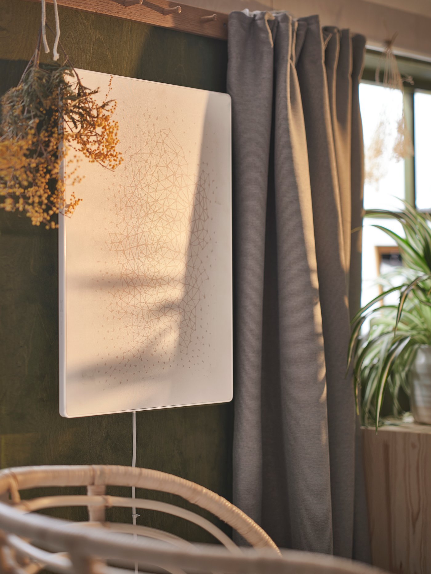 Ein weisser SYMFONISK Rahmen mit WiFi-Speaker vor einer dunkelgrünen Wand. Daneben hängt ein VILBORG verdunkelnder Gardinenschal.
