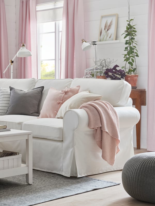 A white EKTORP sofa with cushions and a pink throw in a living room.