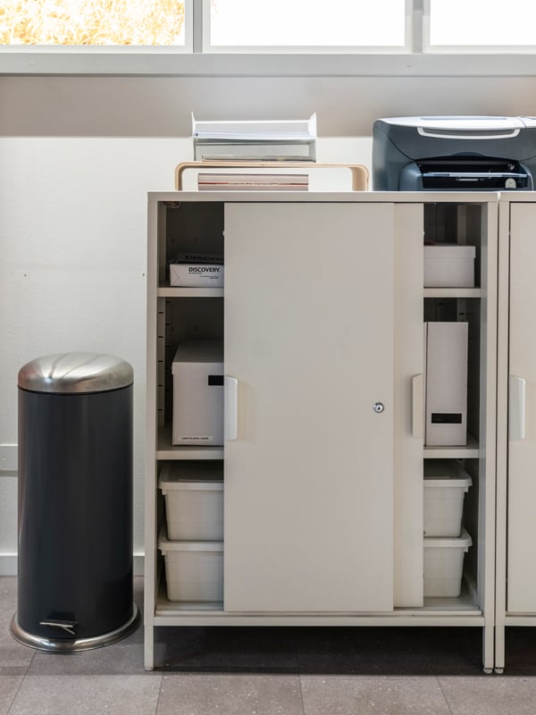 Der TROTTEN Aktenschrank mit den passenden TJENA und SOCKERBIT Boxen steht vor einem Fenster.