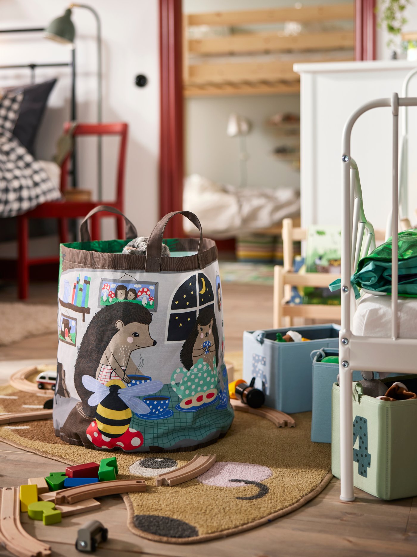Close-up on SKOGSDUVA storage bag on the floor in front of a children’s bed, with toys scattered around it.