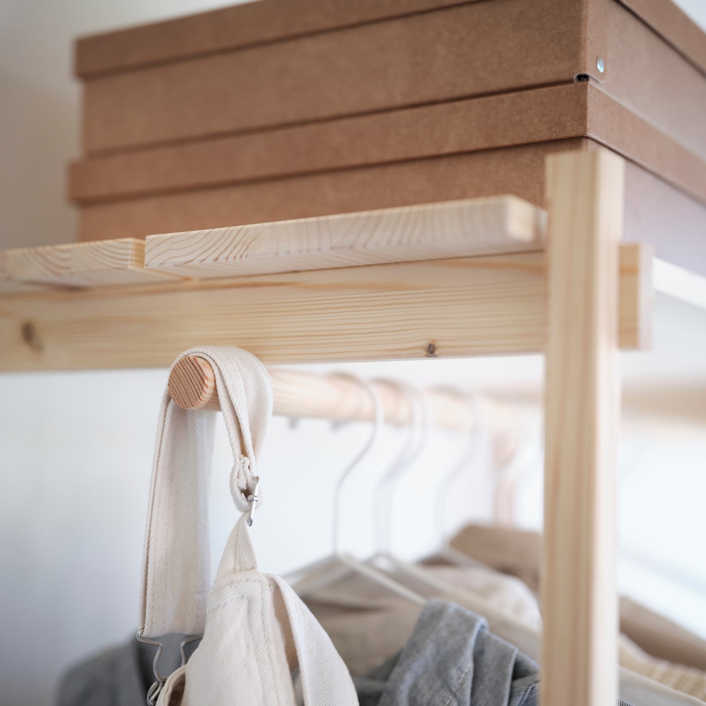 KRONÖREN open wardrobe in pine with hanging rail and top shelf holding clothes and boxes in a bedroom.