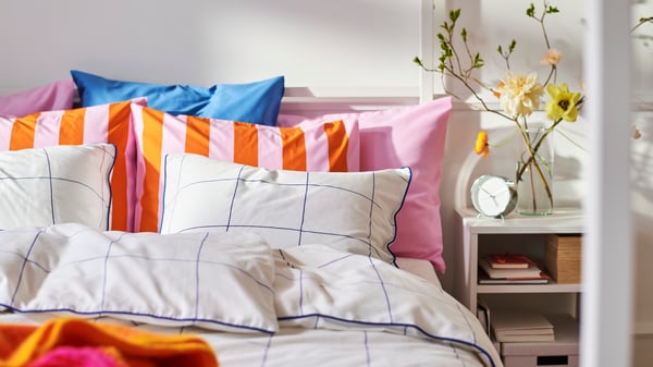 Close-up of bed with a lot of pillows in different patterns and colours. Bedside table on the right.