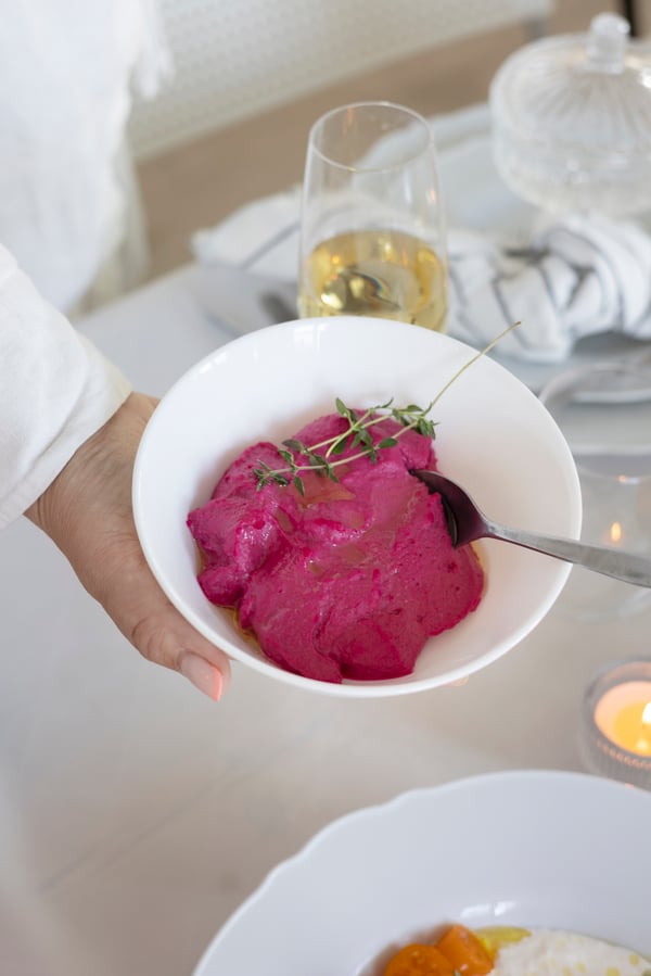 A hand holding a bowl of beetroot hummus 