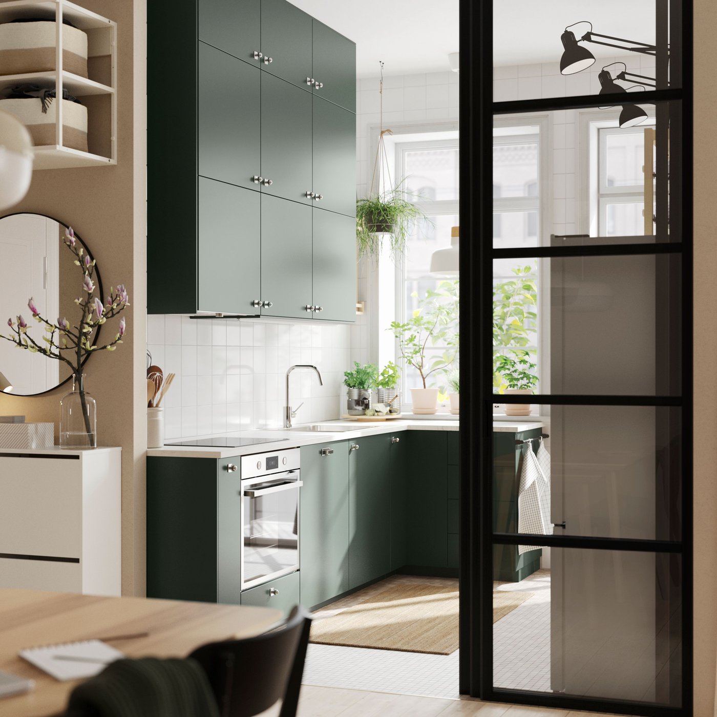 An open kitchen with deep green HAVSTORP kitchen fronts and wall cabinets up to the ceiling, next to a bright living room.