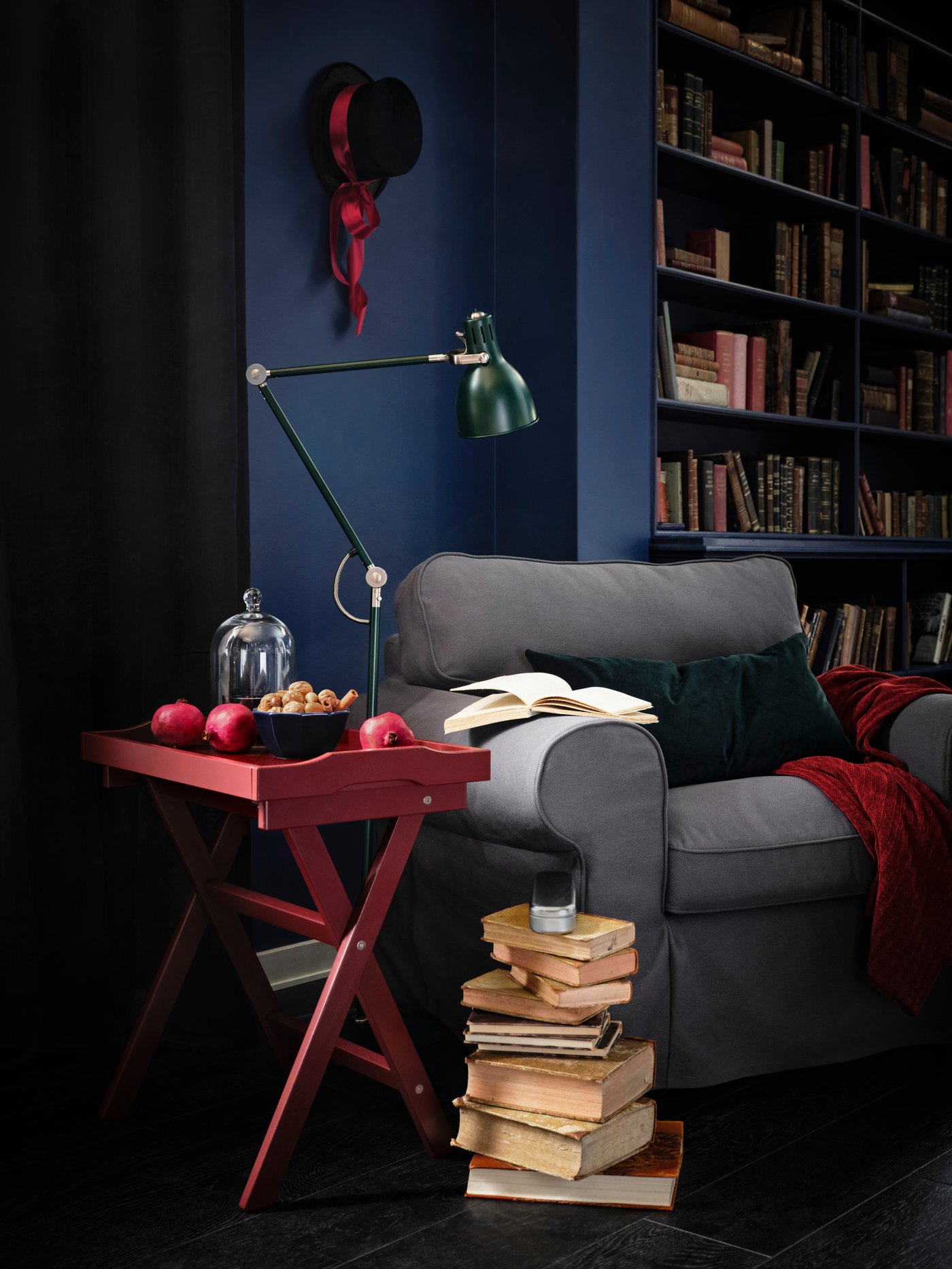 Books are piled up next to a cosy-looking EKTORP armchair with a red table and green lamp stood next to it.