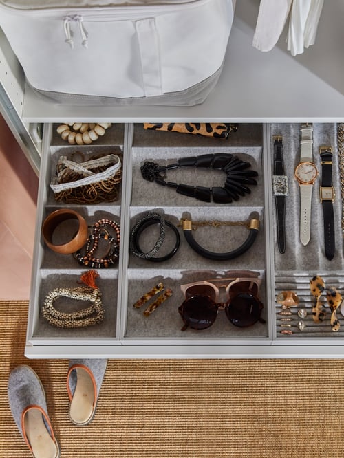 An open wardrobe drawer has light grey inserts, including a KOMPLEMENT insert with four compartments that holds accessories.