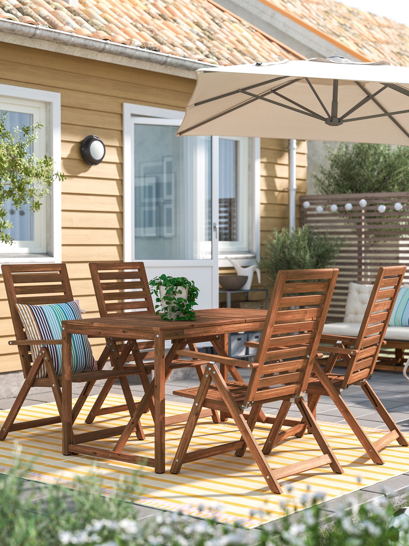 Ombrellone pensile SVALÖN grigio‑beige chiaro che ombreggia una zona pranzo da esterno con tavolo e sedie in legno su terrazza.