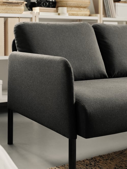 Le côté d’un canapé GLOSTAD gris avec une étagère ouverte EKENABBEN qui contient des dossiers et des paniers de rangement.
