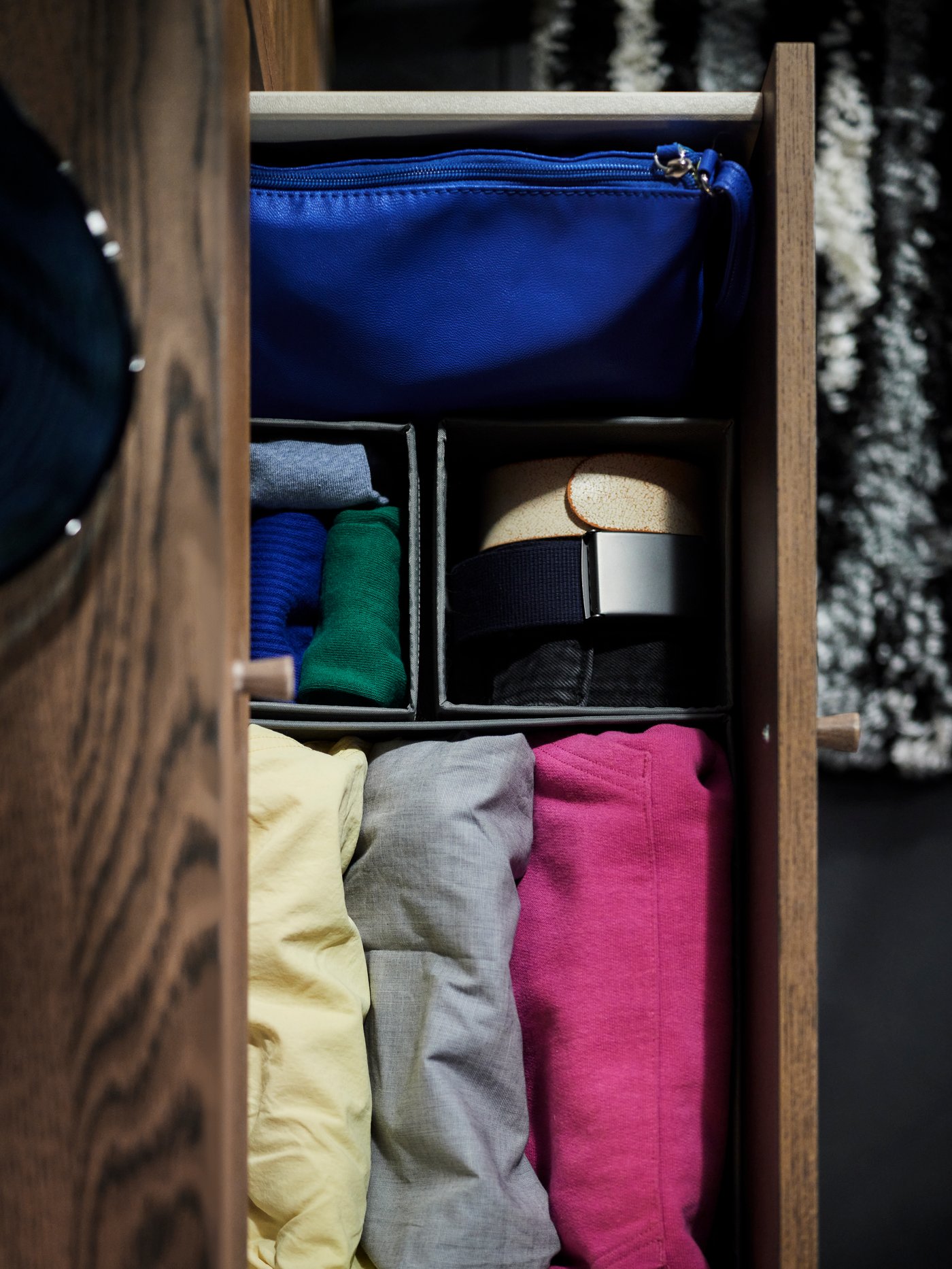 An open top drawer of a brown oak veneer TONSTAD chest with 6 drawers with SKUBB storage boxes holding bright colour clothes.