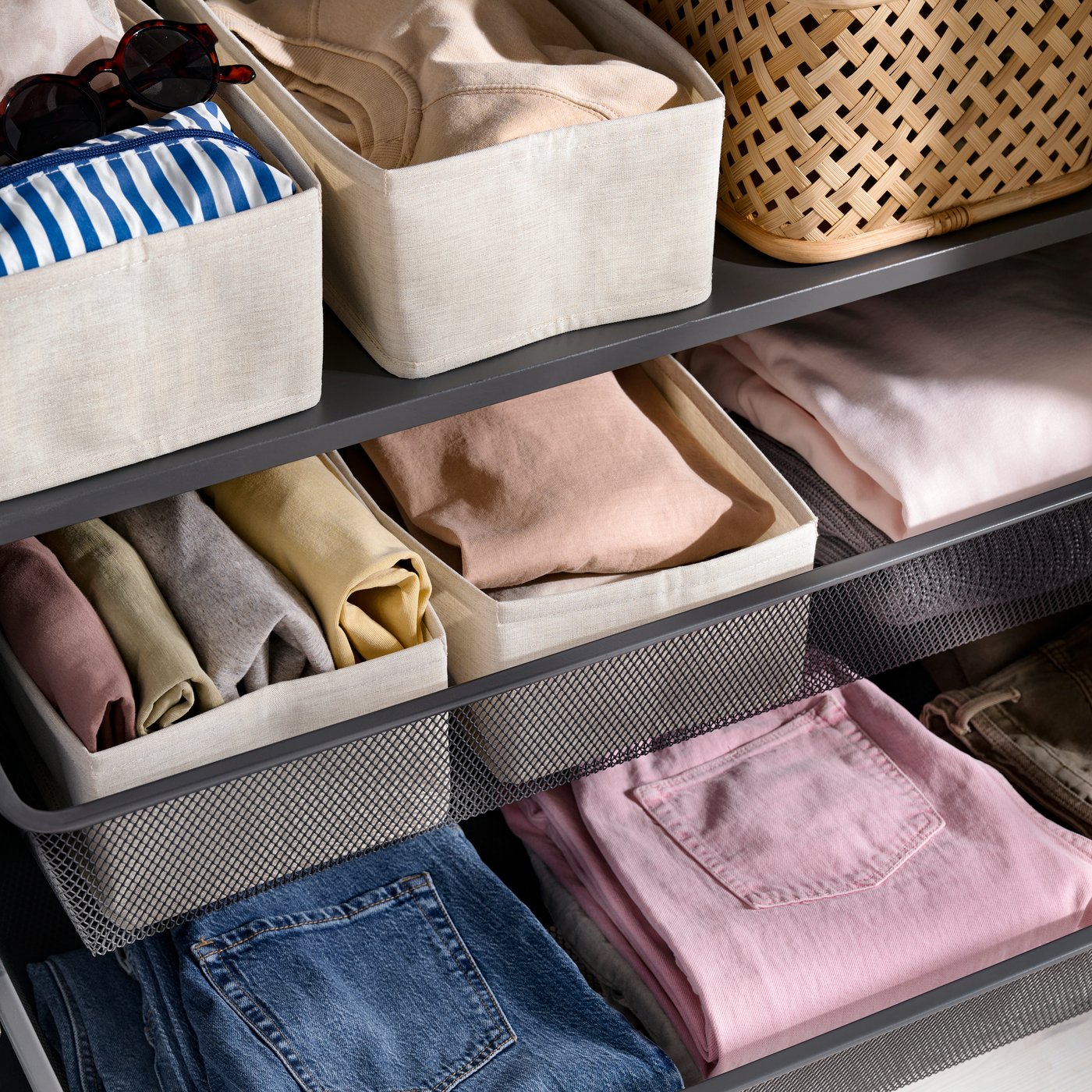 Gros plan sur une armoire PAX gris foncé équipée de paniers en filet KOMPLEMENT et de boîtes PURRPINGLA contenant des vêtements soigneusement pliés.