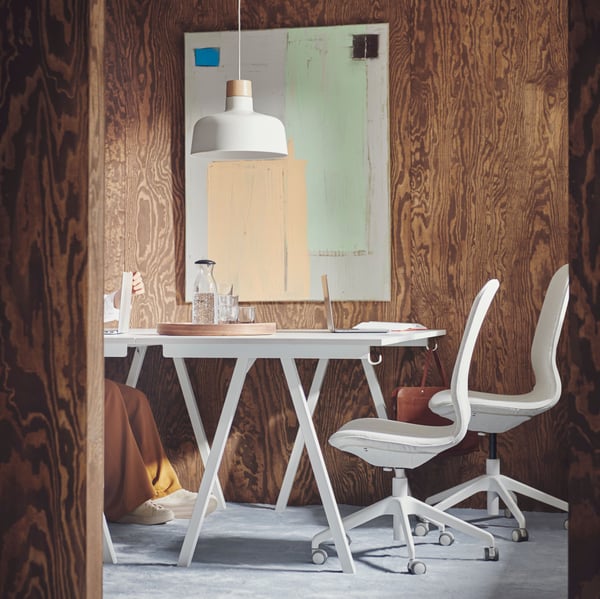 Espace de réunion moquetté et aux murs revêtus de bois brun, avec deux bureaux blancs TROTTEN et deux chaises de bureau LÅNGFJÄLL en beige et blanc.