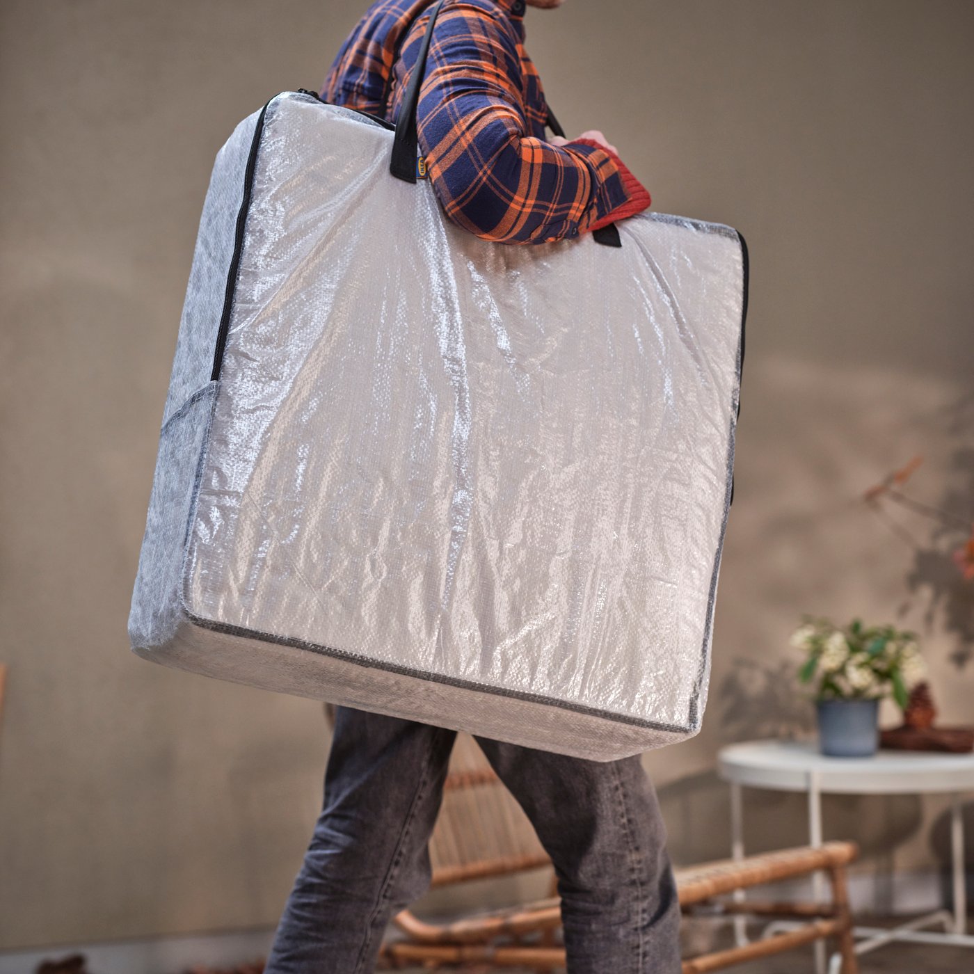 A person with a DIMPA storage bag over their shoulder walks on a terrace near a KROKHOLMEN coffee table.
