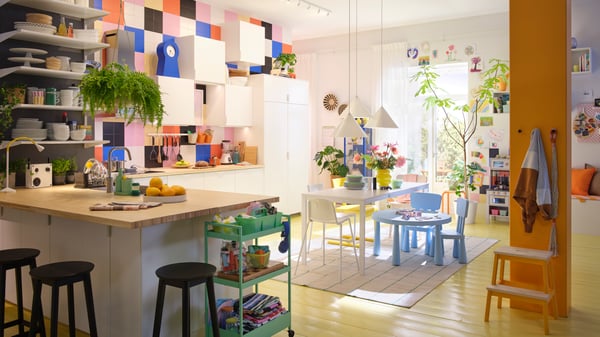 A bright kitchen featuring white VEDDINGE doors, vibrant decor, a wooden table, and potted plants.