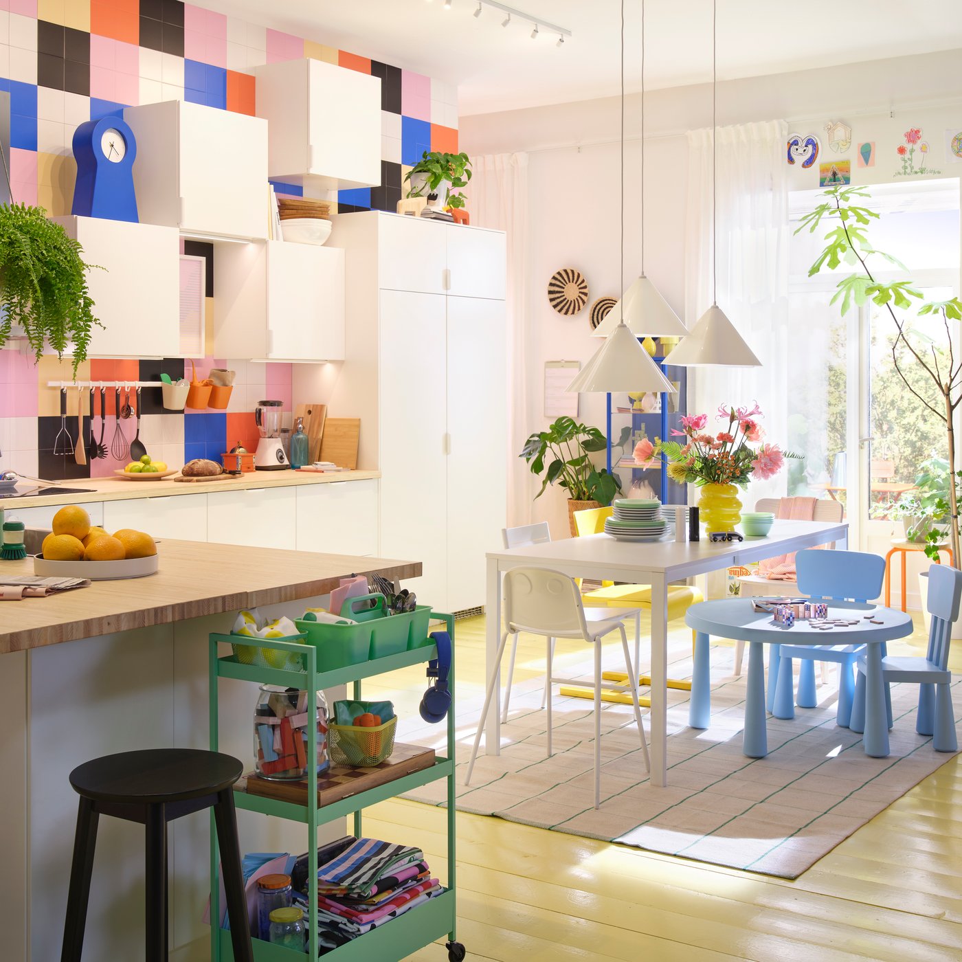 A bright kitchen featuring white VEDDINGE doors, vibrant decor, a wooden table, and potted plants.