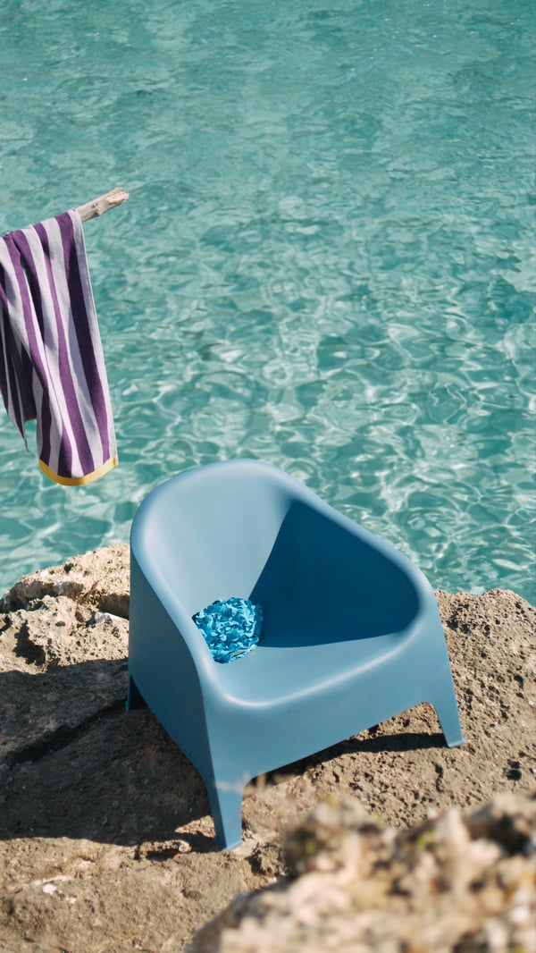 Ein Kunsstoff-Sessel in blau steht am Strand direkt am Wasser.