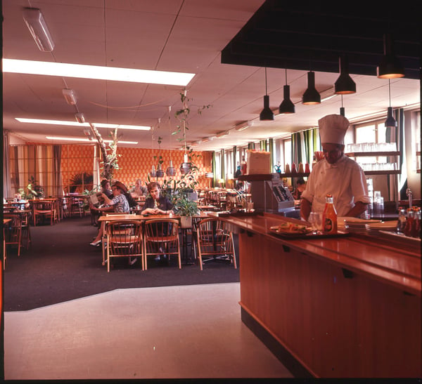 A chef in a high chef’s hat stands behind a counter in an IKEA restaurant sometime in the 1960s.