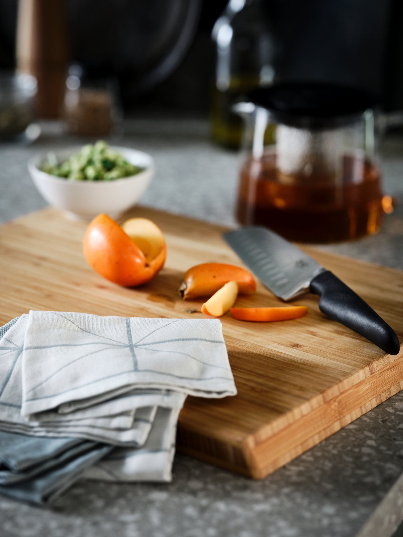 A terrazzo-style worktop with an APTITLIG chopping board, on which lie a blue SANDVIVA tea towel and a black VÖRDA knife.