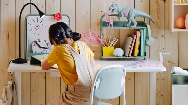 Close-up of young girl at white school desk with green writing board and whiteboard in childrens bedroom with wood walls.