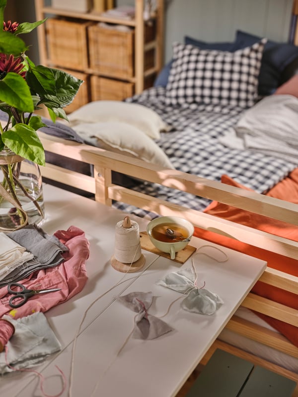 A white HAUGA drop leaf extendable table at the end of a TARVA bed with anthracite white check EKTANDVINGE bed linen on it.