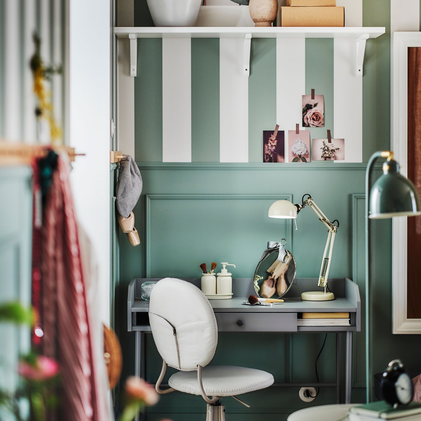 Ett grått HAUGA skrivbord i hörnet av ett grönt rum med en beige BJÖRKBERGET snurrstol framför och en FORSÅ arbetslampa ovanpå.
