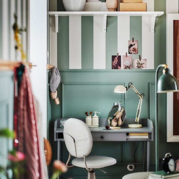 A grey HAUGA desk in the corner of a green room with a beige BJÖRKBERGET swivel chair in front and a FORSÅ work lamp on top.