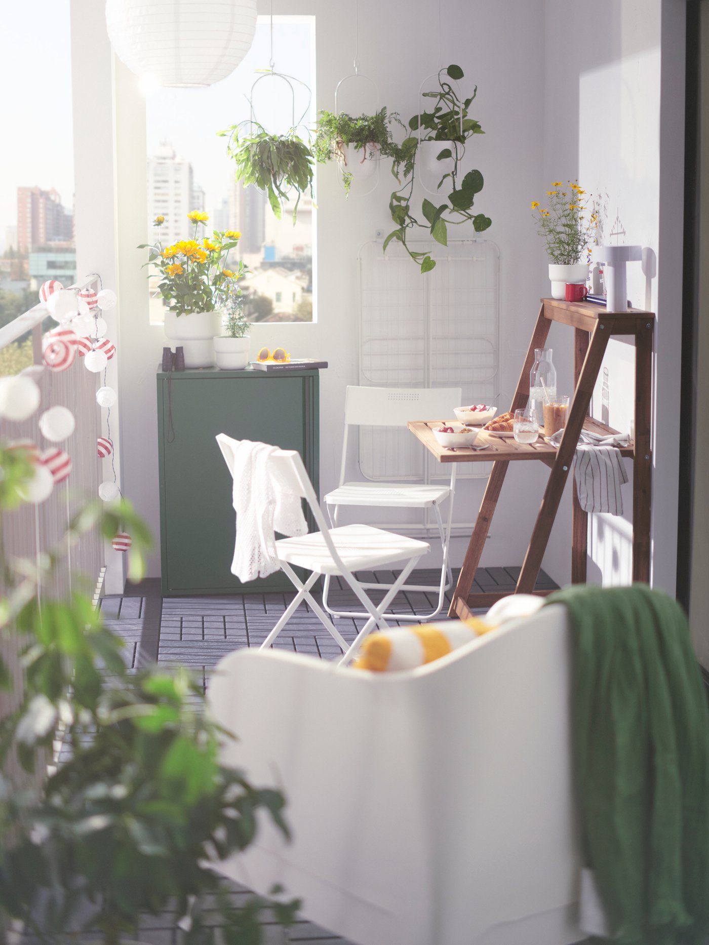 Zona de balcón con un sillón SKARPÖ blanco en primer plano, y una mesa plegable, una silla y un armario al fondo.