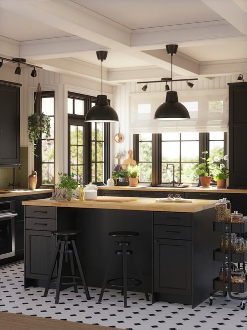 A kitchen with DALFRED bar stools next to black cabinets with KARLBY worktops beside a trolley and black pendant lamps above.