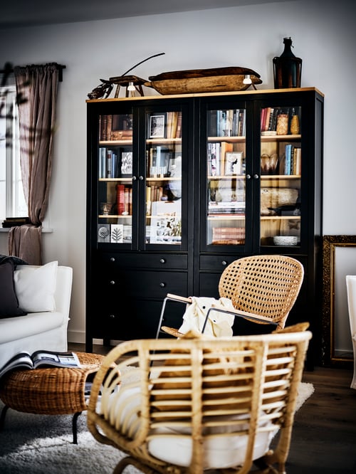 Two black HEMNES glass-door cabinets filled with books, in a country-style living room by two armchairs and a sofa.
