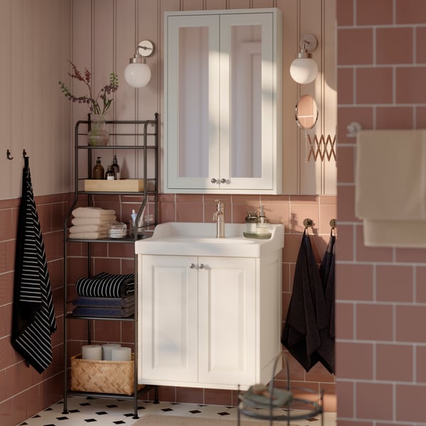 Une salle de bains équipée d’un meuble pour salle de bains avec lavabo et deux tiroirs TÄNNFORSEN blanc, à côté d’une tablette métallique où se trouvent des serviettes.