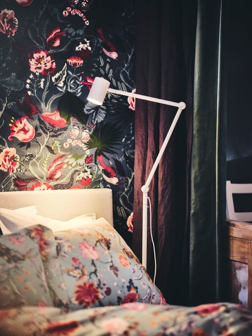 Schlafbereich mit einer NYMÅNE Stand-/Leseleuchte und FILODENDRON Meterware an der Wand hinter dem Bett.