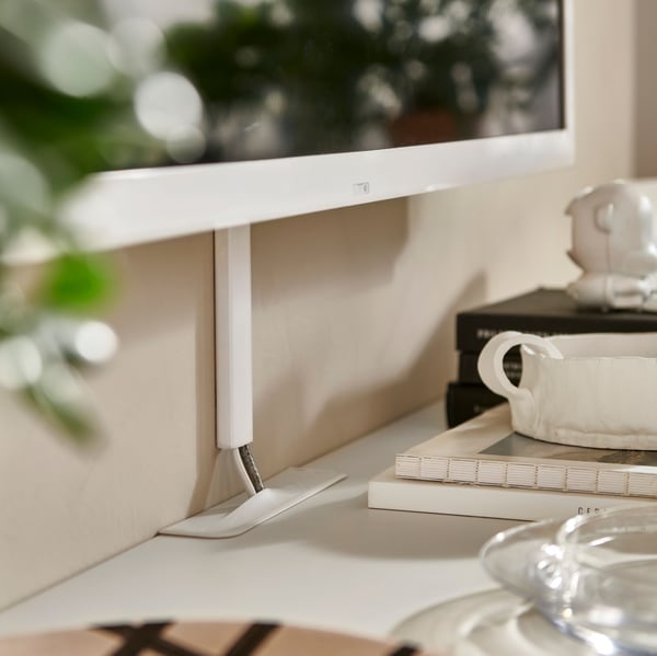 Cables from a wall-mounted TV enter a white BESTÅ TV bench with doors through a cable outlet on the top of the bench.